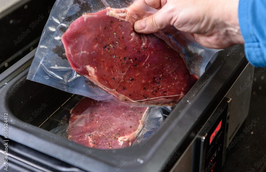 A person places a sirloin steak inside a vacuum sealed bag into a sous vide water bath to cook at 55C.