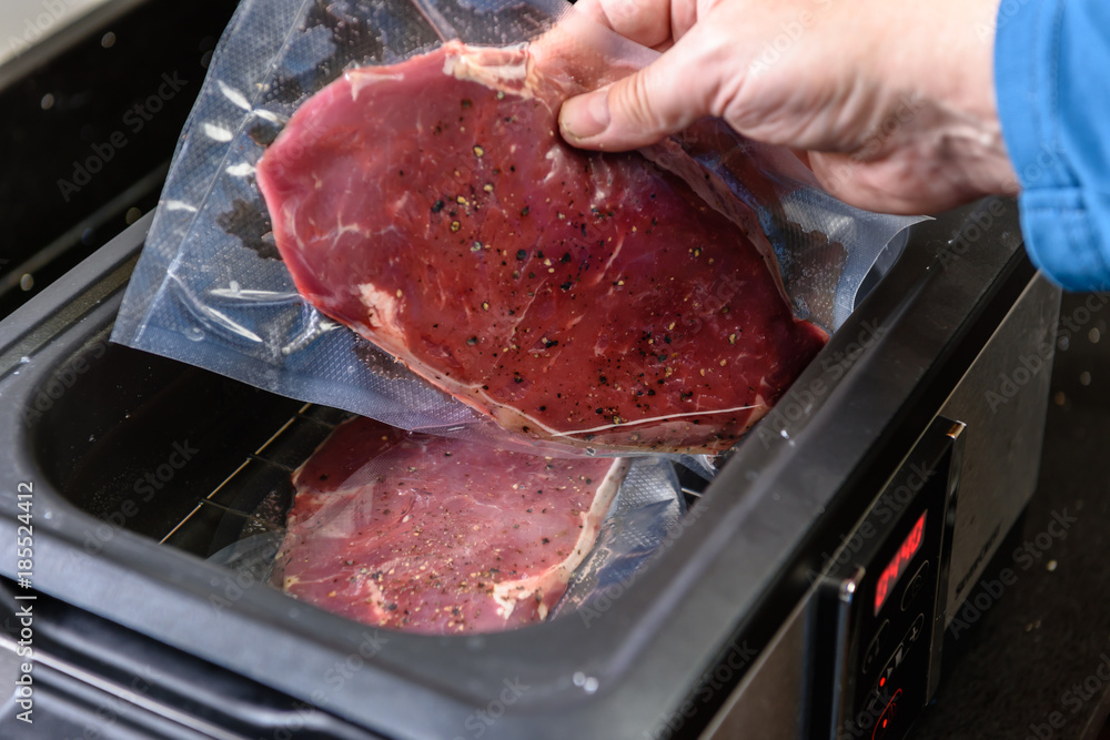 A person places a sirloin steak inside a vacuum sealed bag into a sous vide water bath to cook at 55C.